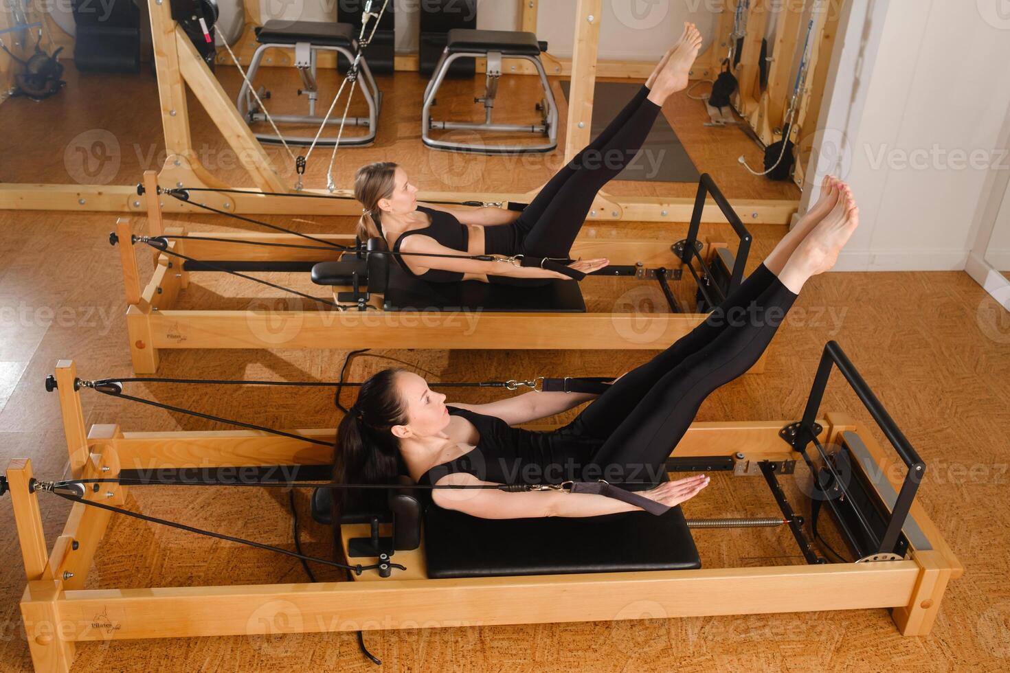 Two women balance on a pilates reformer machine in the gym photo