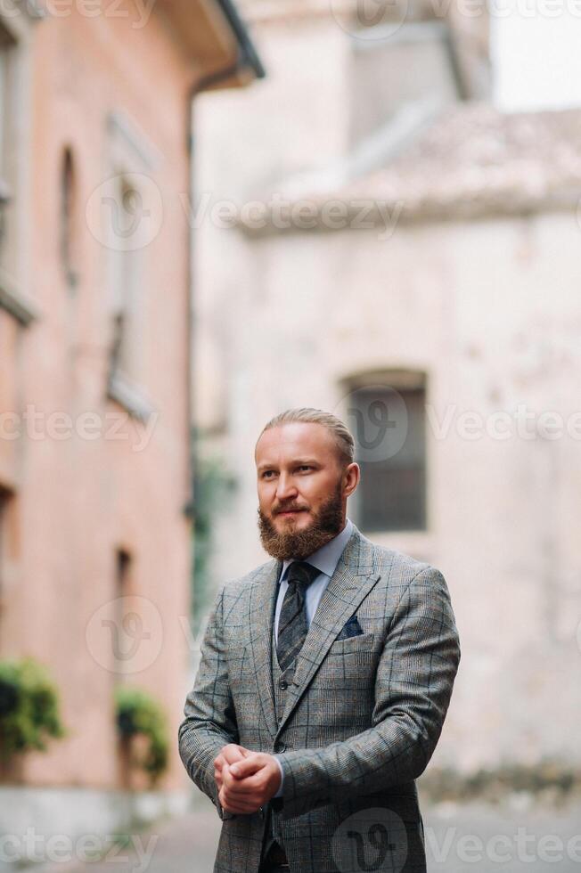 A man with a beard in a strict grey three-piece suit with a tie in the old town of Sirmione, a Stylish man in a grey suit in Italy photo