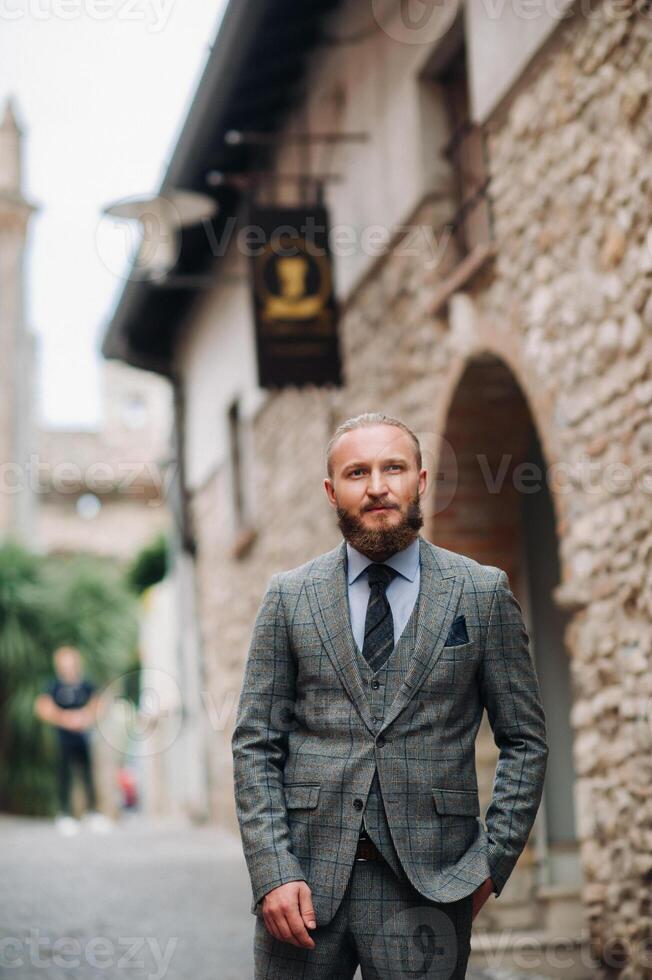 A man with a beard in a strict grey three-piece suit with a tie in the old town of Sirmione, a Stylish man in a grey suit in Italy photo