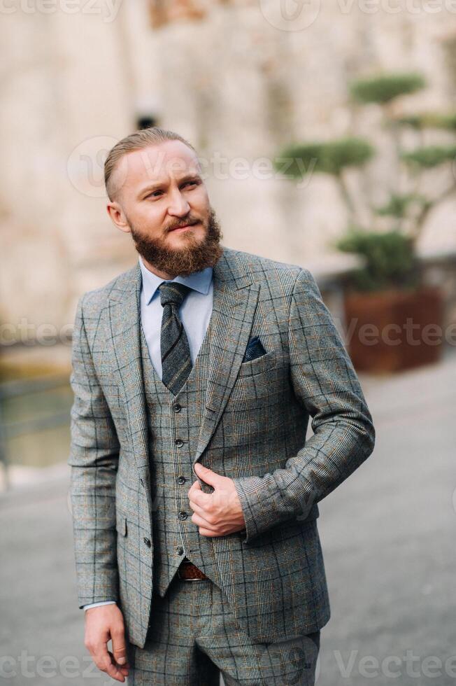 A man with a beard in a strict grey three-piece suit with a tie in the old town of Sirmione, a Stylish man in a grey suit in Italy photo
