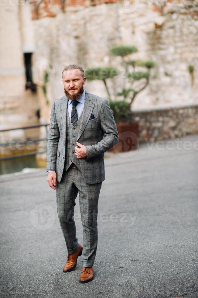 A man with a beard in a strict grey three-piece suit with a tie in the old town of Sirmione, a Stylish man in a grey suit in Italy photo