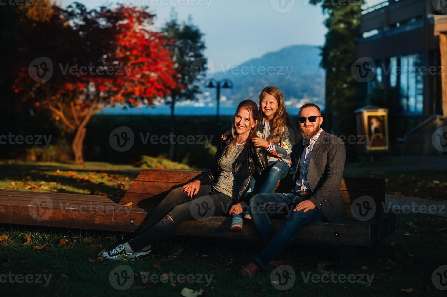 A happy family of three sits on a bench at a Sunny autumn sunset in Austria's Old town.A family poses in a small Austrian town against the backdrop of the Austrian Alps.Europe.Felden am see photo