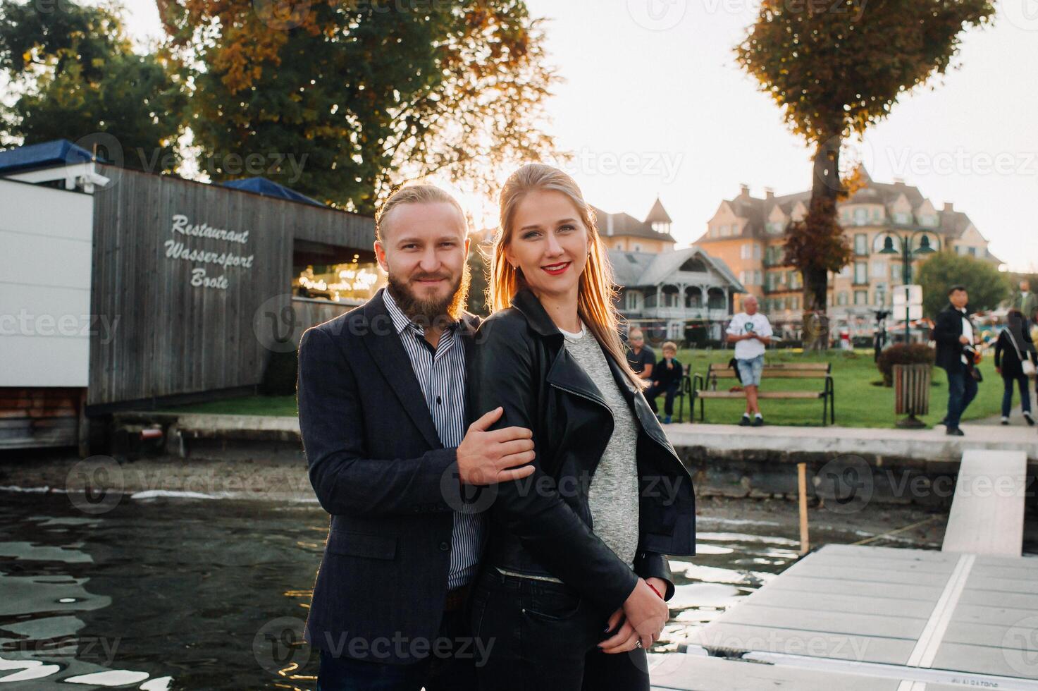a family of two stands on a pier in Austria's old town at sunset .A man and a woman embrace on the embankment of a small town in Austria.Europe.Felden am Werten see photo