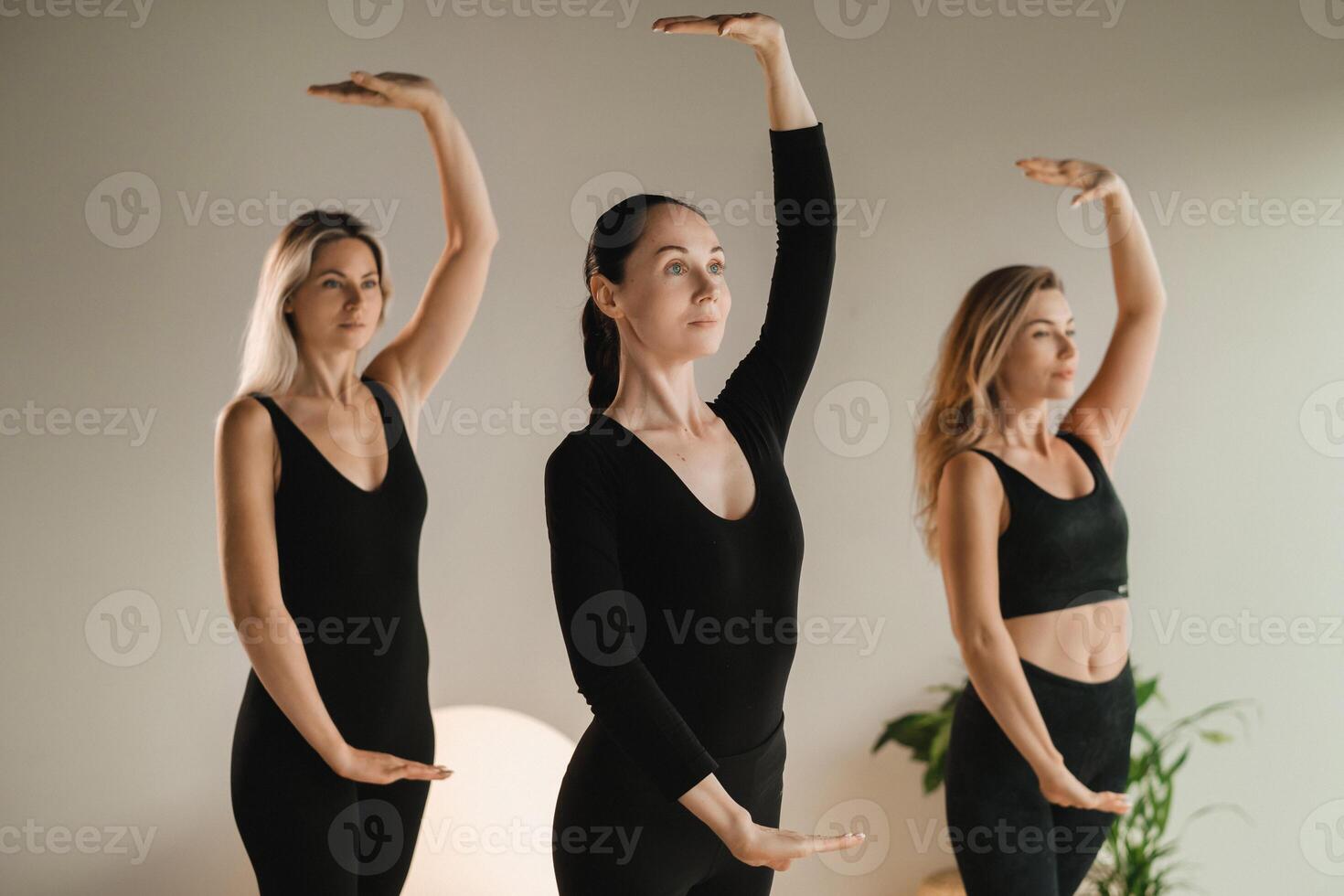A group of girls in black doing yoga poses indoors. Women are engaged in fitness photo