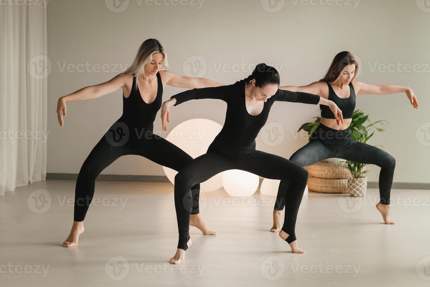 A group of girls in black doing yoga poses indoors. Women are engaged in fitness photo
