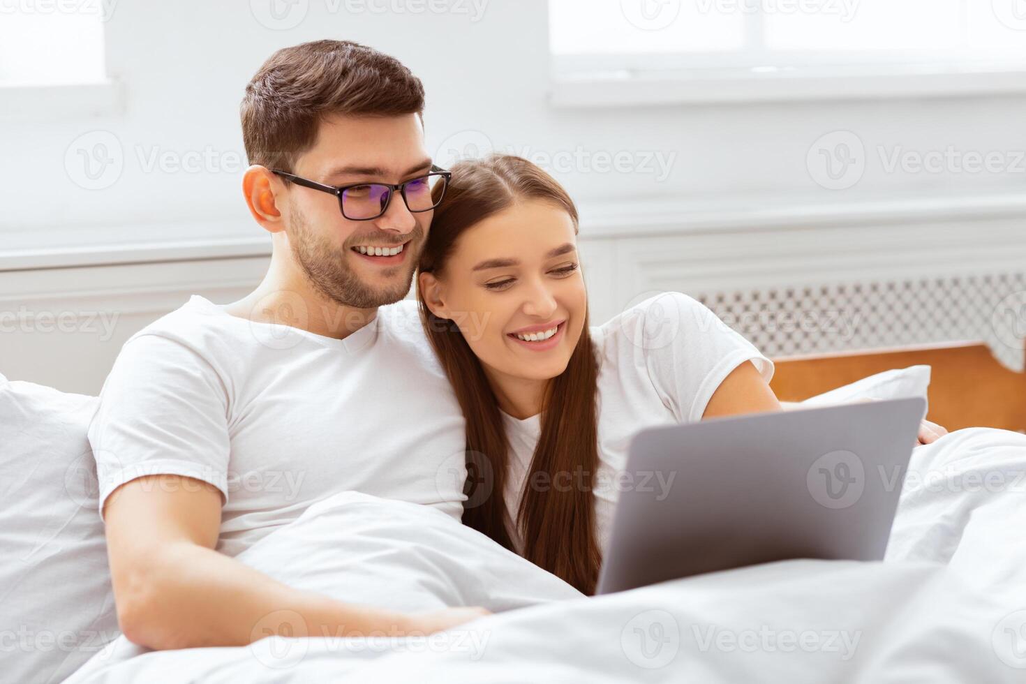 Weekend Leisure. Happy Spouses Using Laptop Watching Movie Sitting In Bed At Home. Selective Focus photo