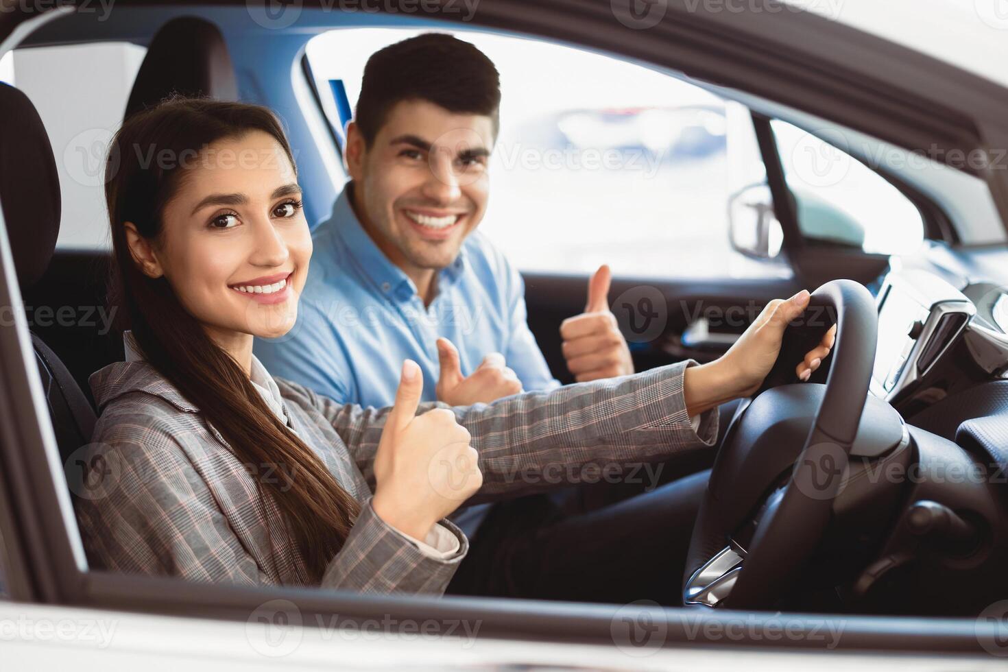 Great Car. Happy Couple Gesturing Thumbs Up Sitting In New Auto Buying Automobile In Dealership Store. Selective Focus photo