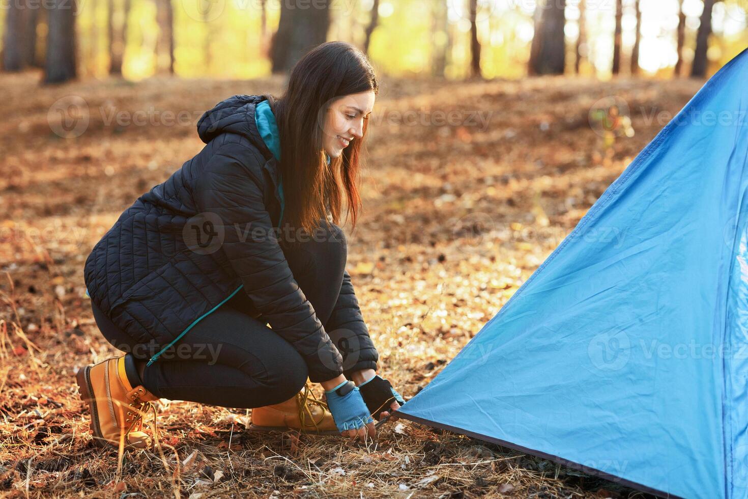 Happy adventurous girl setting camp in autumn forest, placing tent, empty space photo