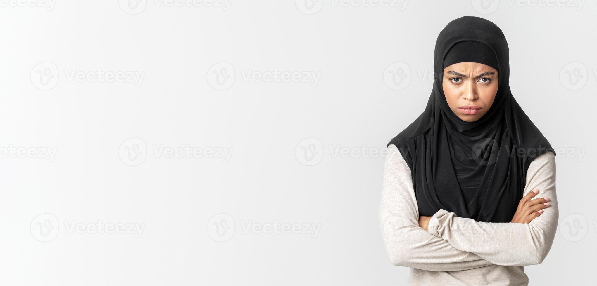 Offended afro muslim woman in hijab standing with folded arms over gray background, frowning and looking at camera, free space photo