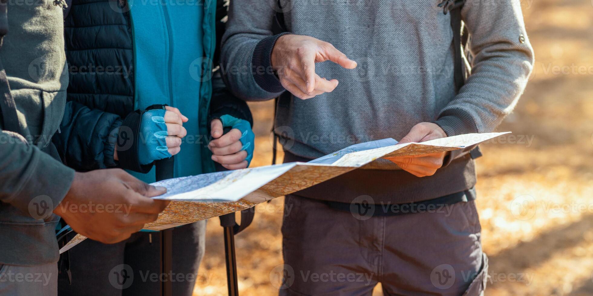 Cropped of multiracial friends with backpacks looking at map, hiking in autumn forest photo