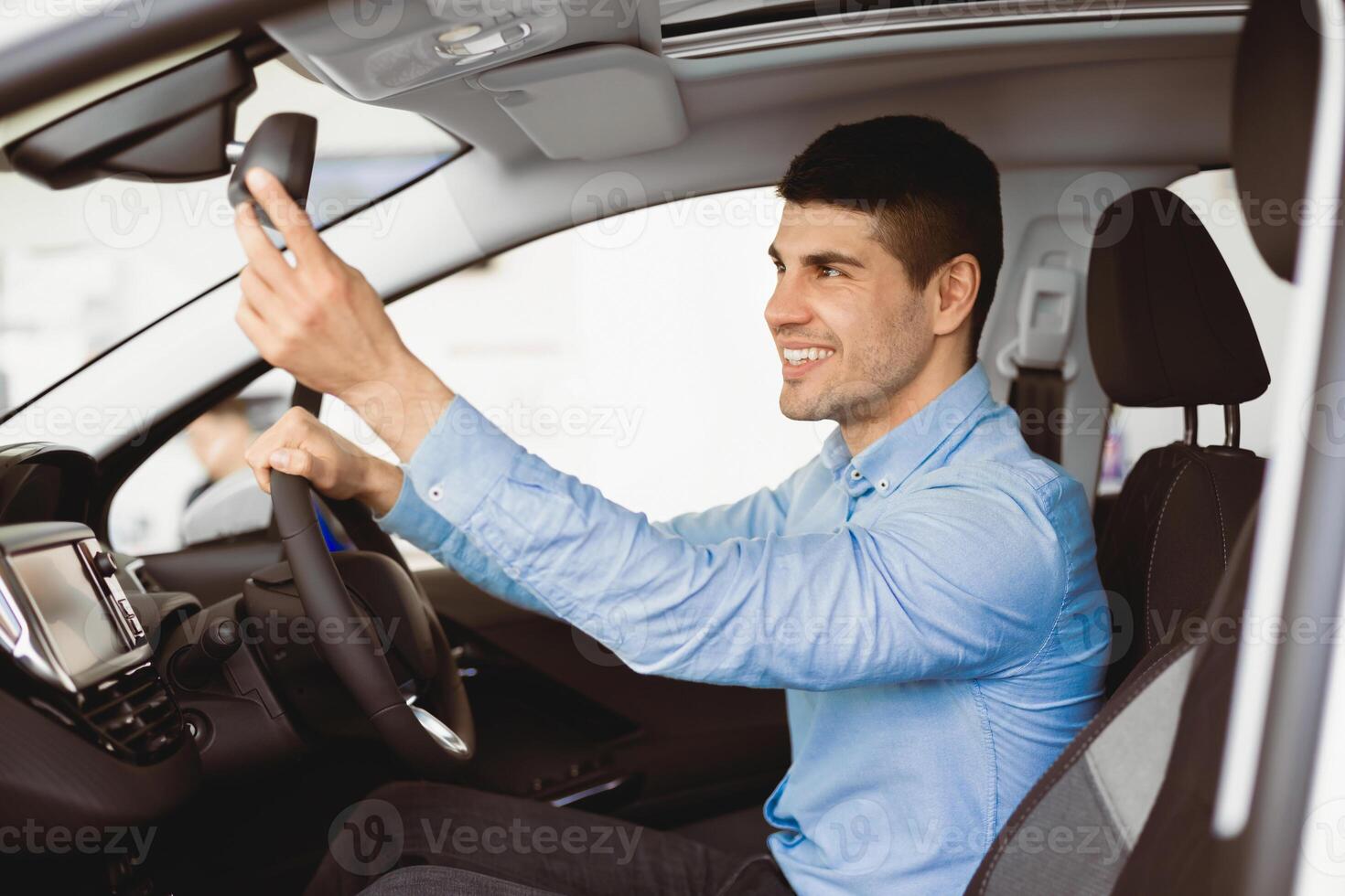 Young Driver. Happy Guy Checking Mirrors Sitting In Driver's Seat Testing Buying Auto In Dealership Store, Side View photo