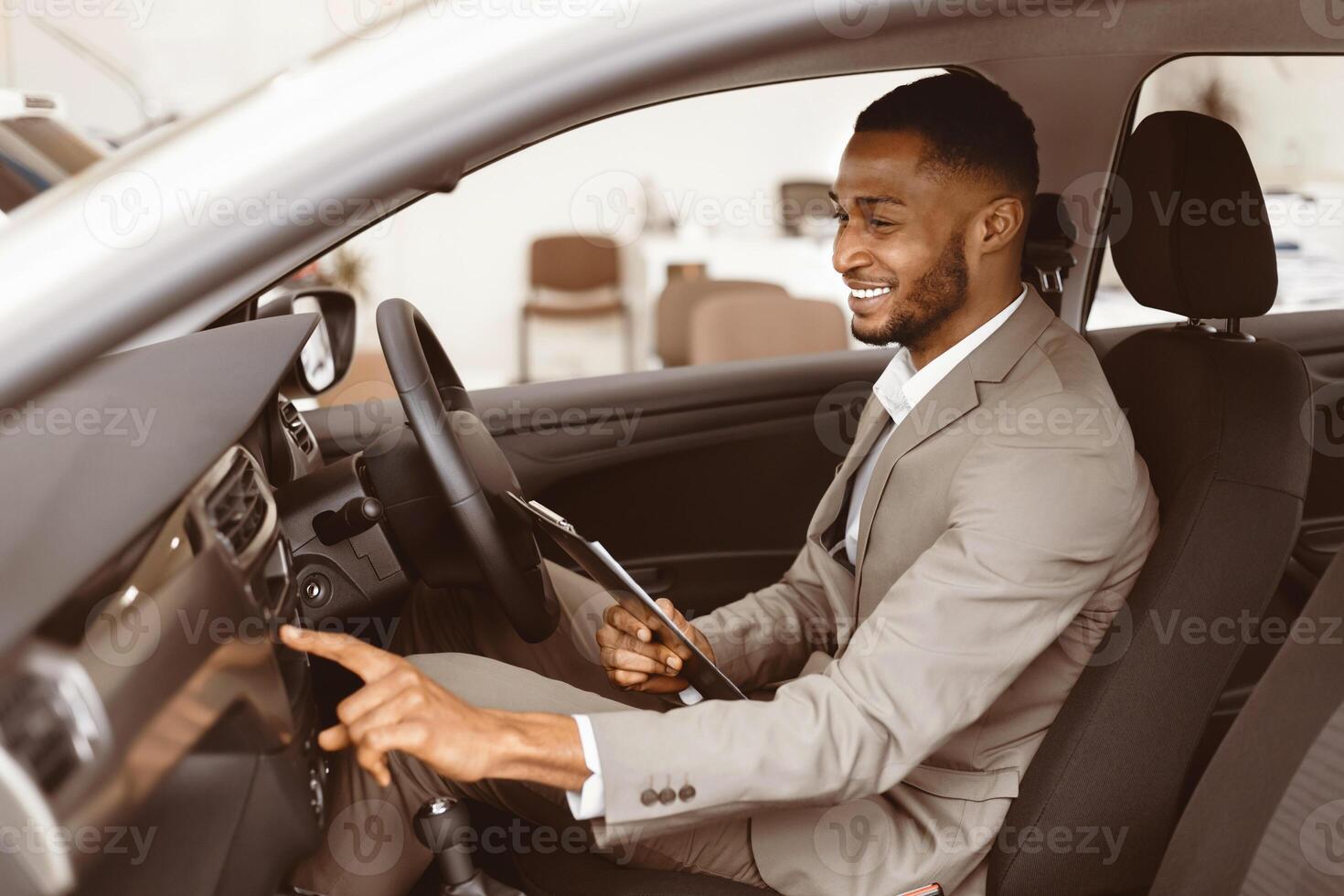 Car Insurance. Afro Agent Man Checking Vehicle Taking Notes Sitting In Automobile In Dealership Showroom. Selective Focus photo