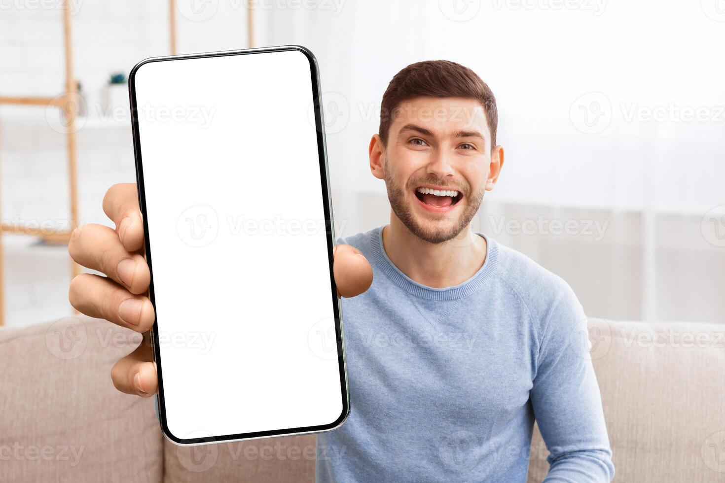 Hello. Cheerful Guy Waving Hand Smiling Looking At Camera Sitting On Couch Indoor. photo