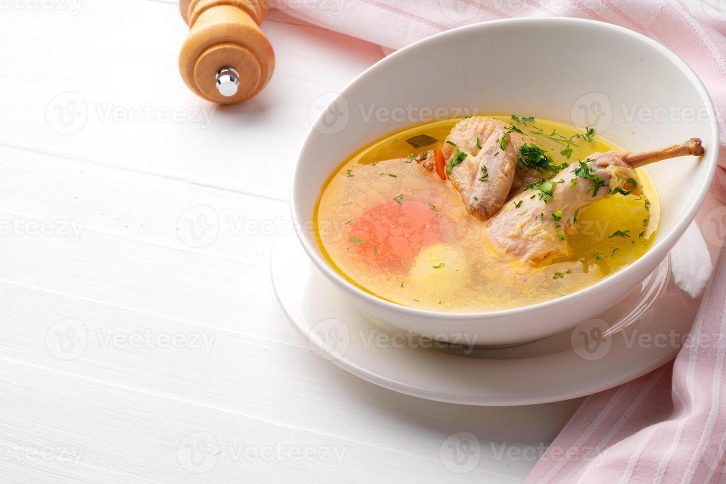 Chicken soup with vegetables in white bowl on wooden table photo