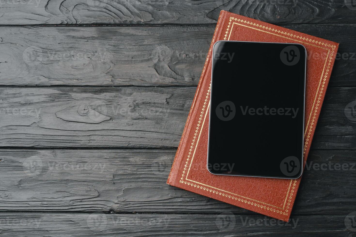 Digital tablet with black screen and book on wooden table photo