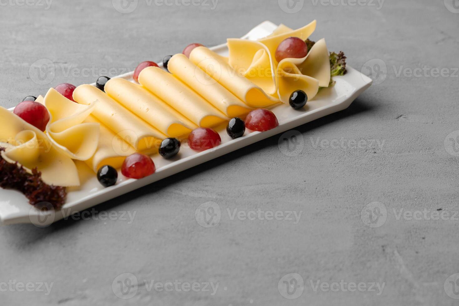 Cheese platter with grapes and black olives on gray background photo