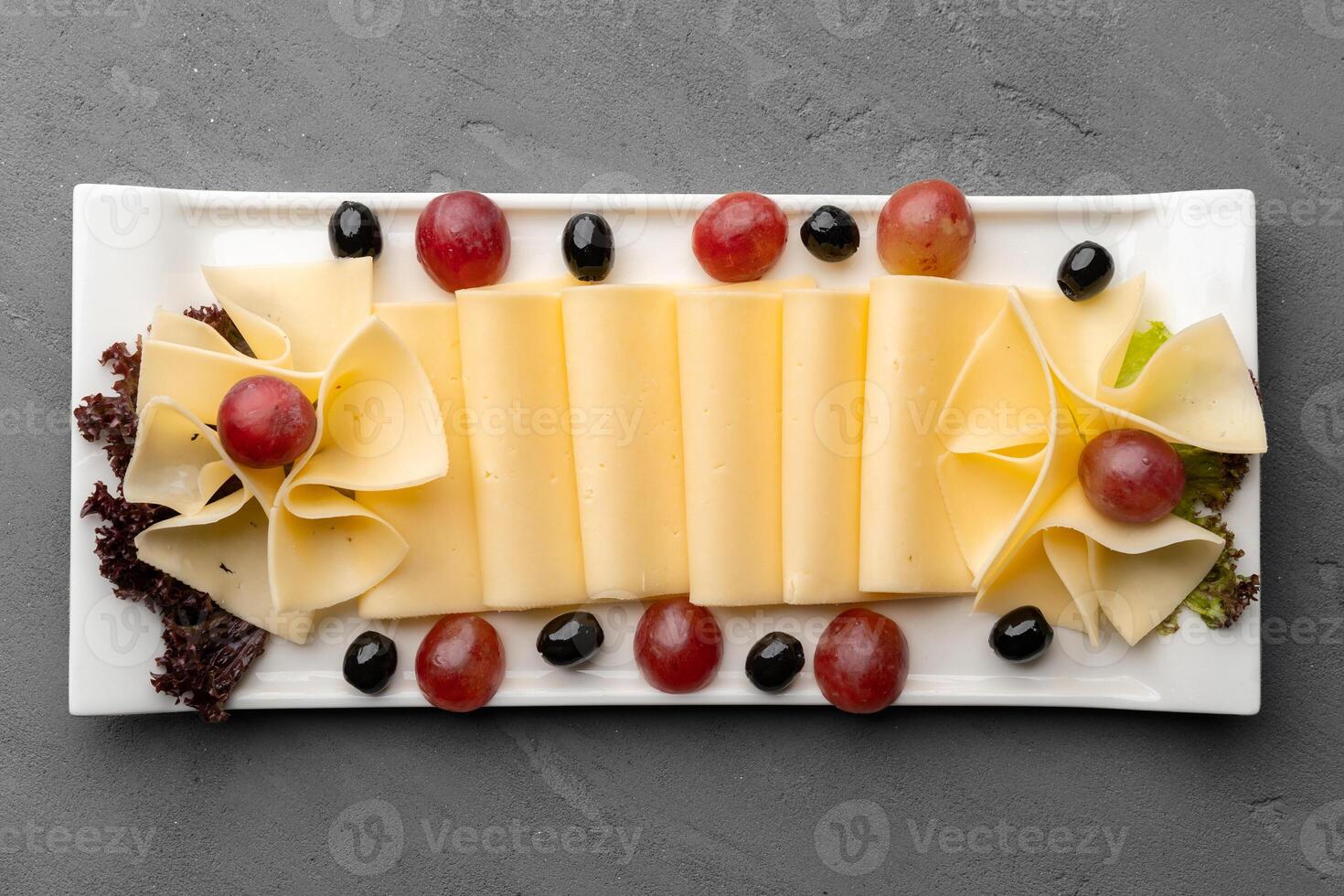 Cheese platter with grapes and black olives on gray background photo