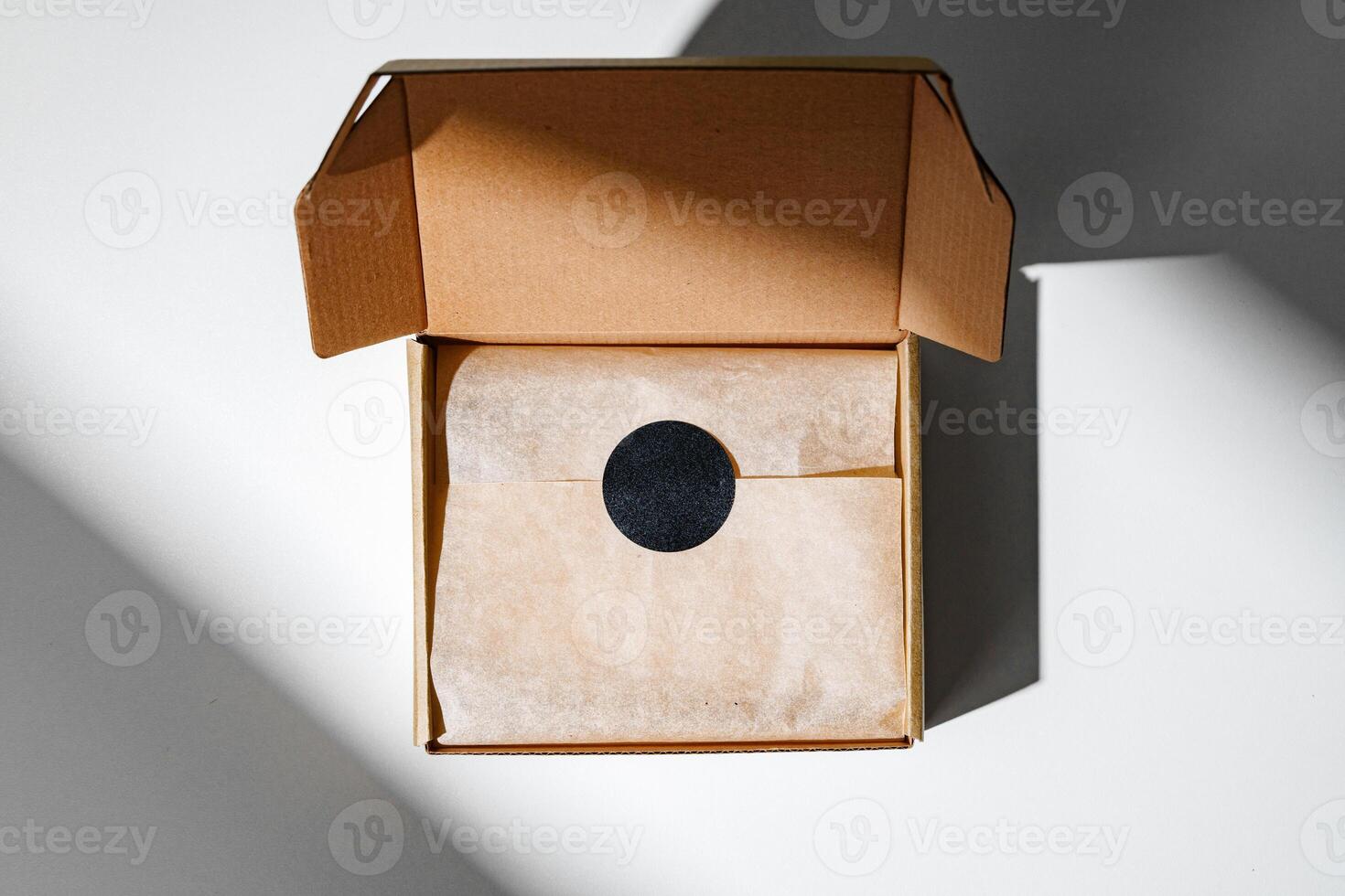 A small, empty cardboard box with unwrapped parchment resting inside on a bright, sunlit table photo
