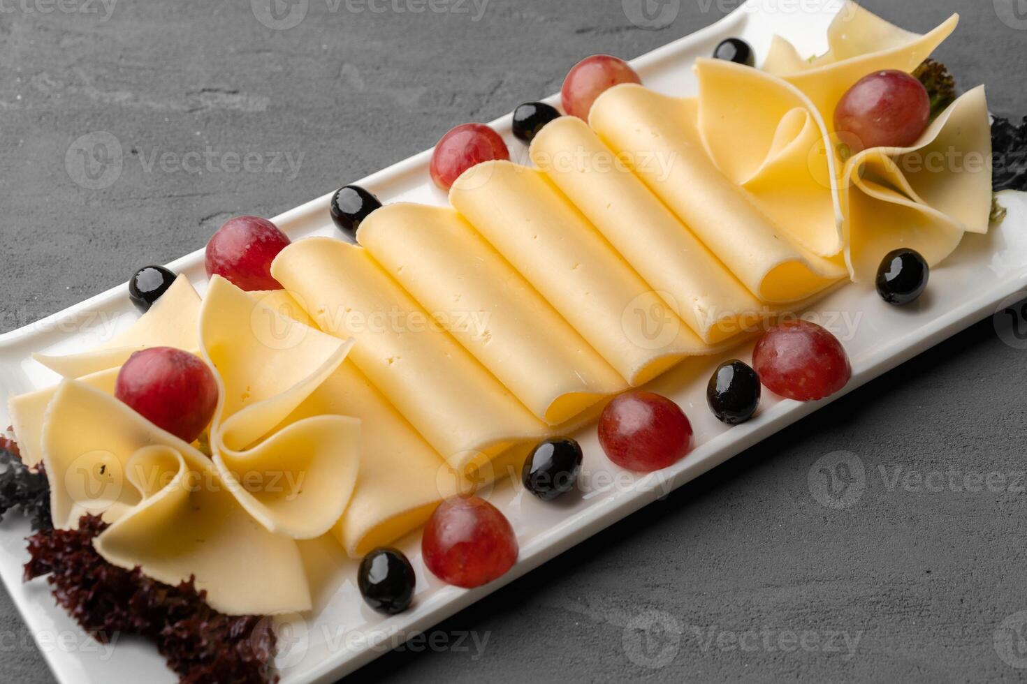 Cheese platter with grapes and black olives on gray background photo