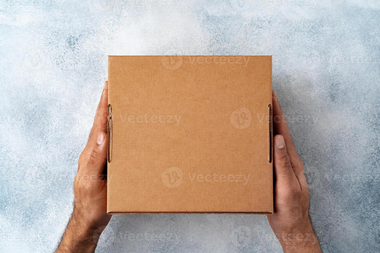 Parcel cardboard box in a man hands on a gray table background photo