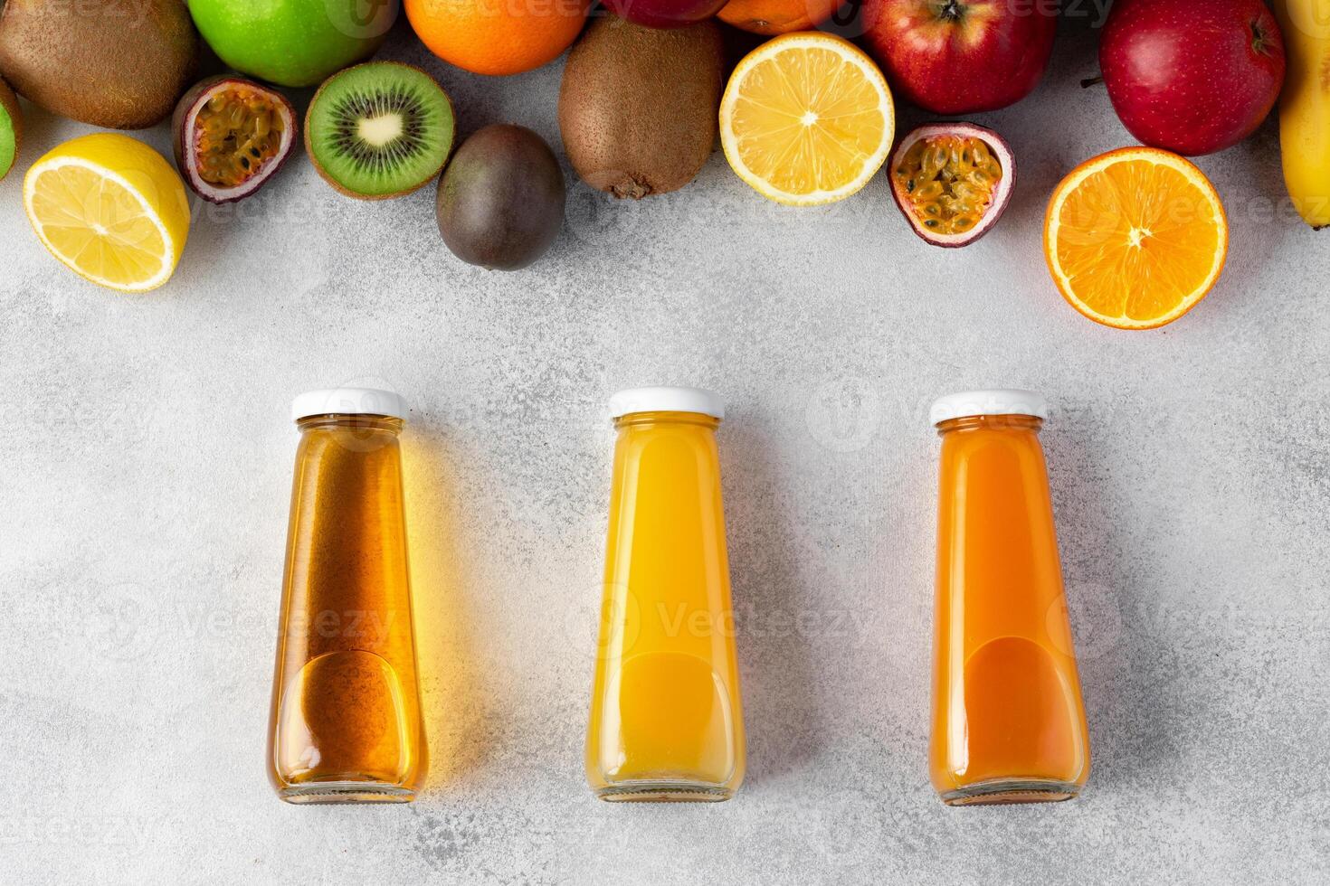 Various fruits and freshly squeezed fruits juice in bottle on gray background photo
