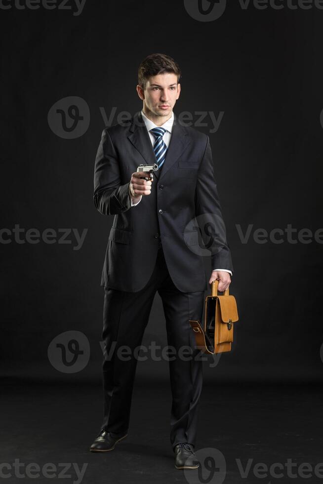 Young man in formal wear holding brown leather bag on black background photo