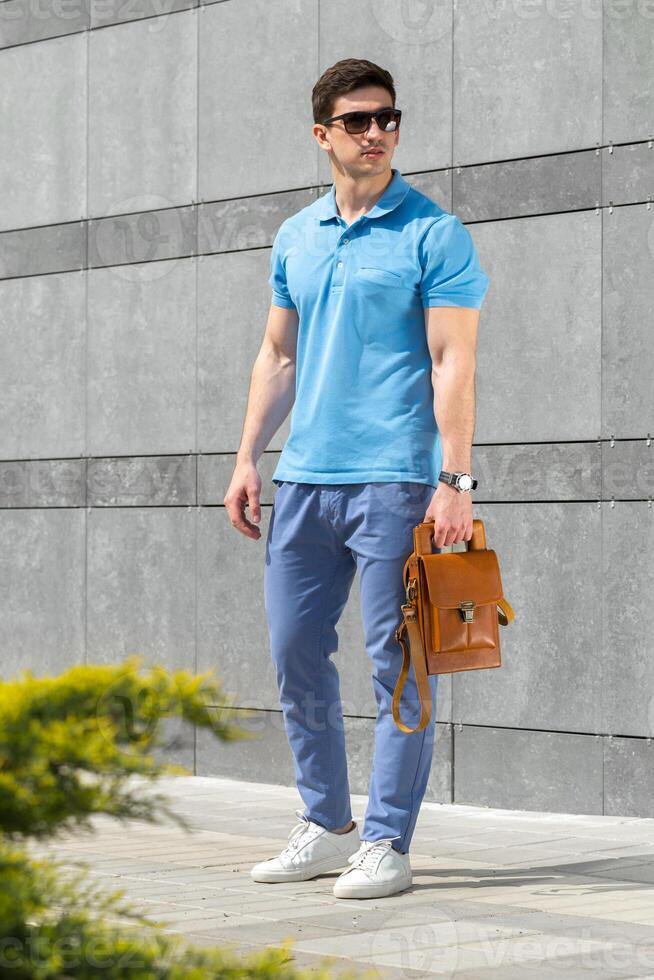 Young man in casual outfit holding brown leather bag in the street photo