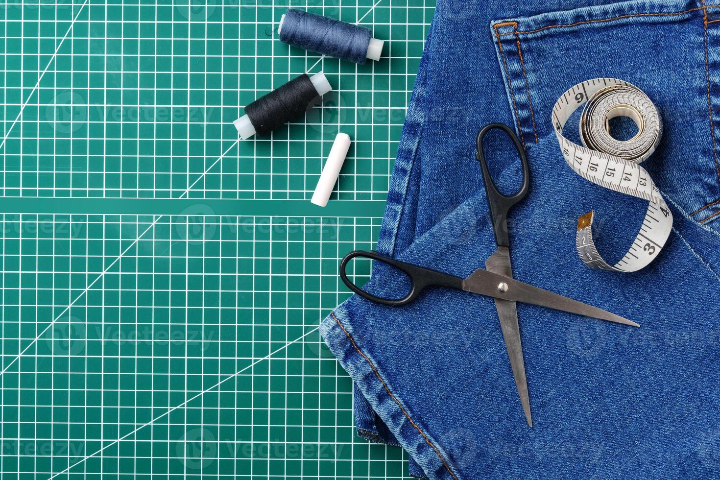 Sewing tools on a cutting mat with denim and thread spools in a craft workspace photo
