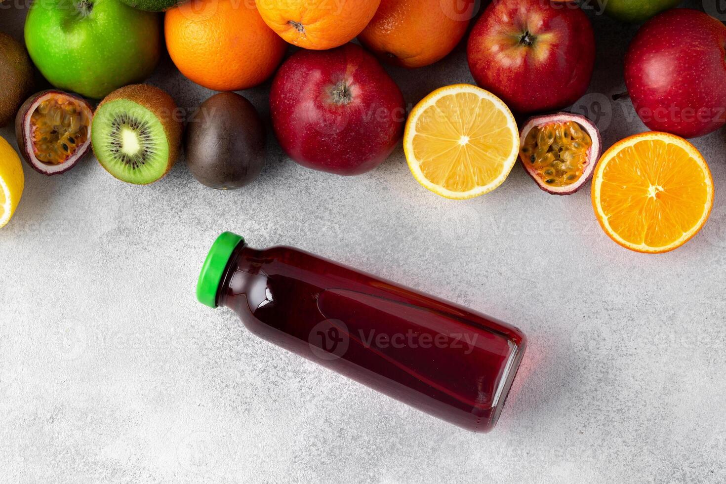 Various fruits and freshly squeezed fruits juice in bottle on gray background photo