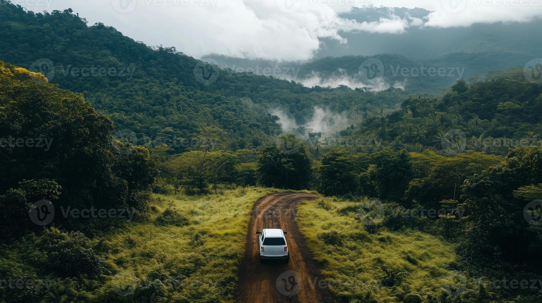 A solitary vehicle travels along a winding dirt road through lush mountains and misty valleys on an overcast day in the countryside photo