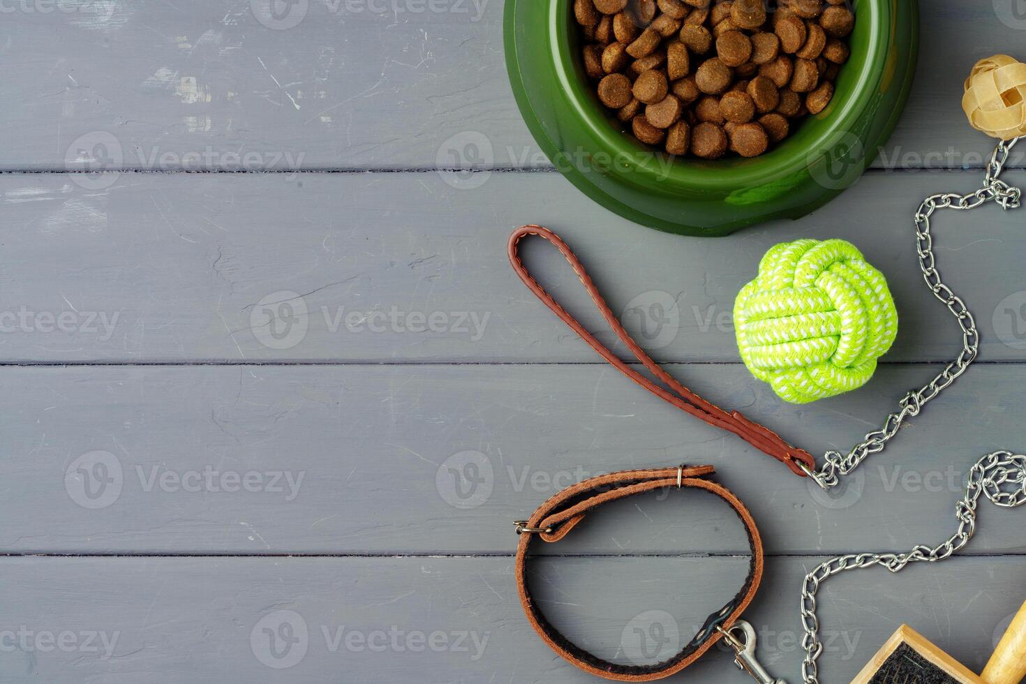 Bowl with dry pet food and toys on gray wooden background photo