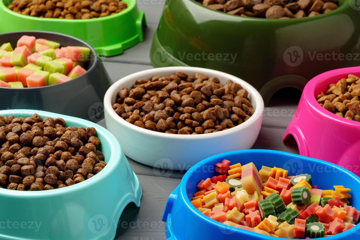 Various pet bowls with dry food on gray wooden background photo