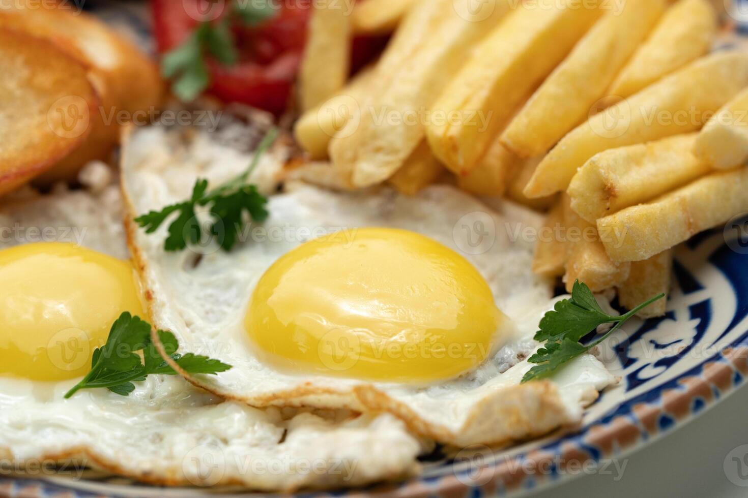 Breakfast plate with fried eggs, sausage, tomatoes, and fries served on a decorative blue plate photo
