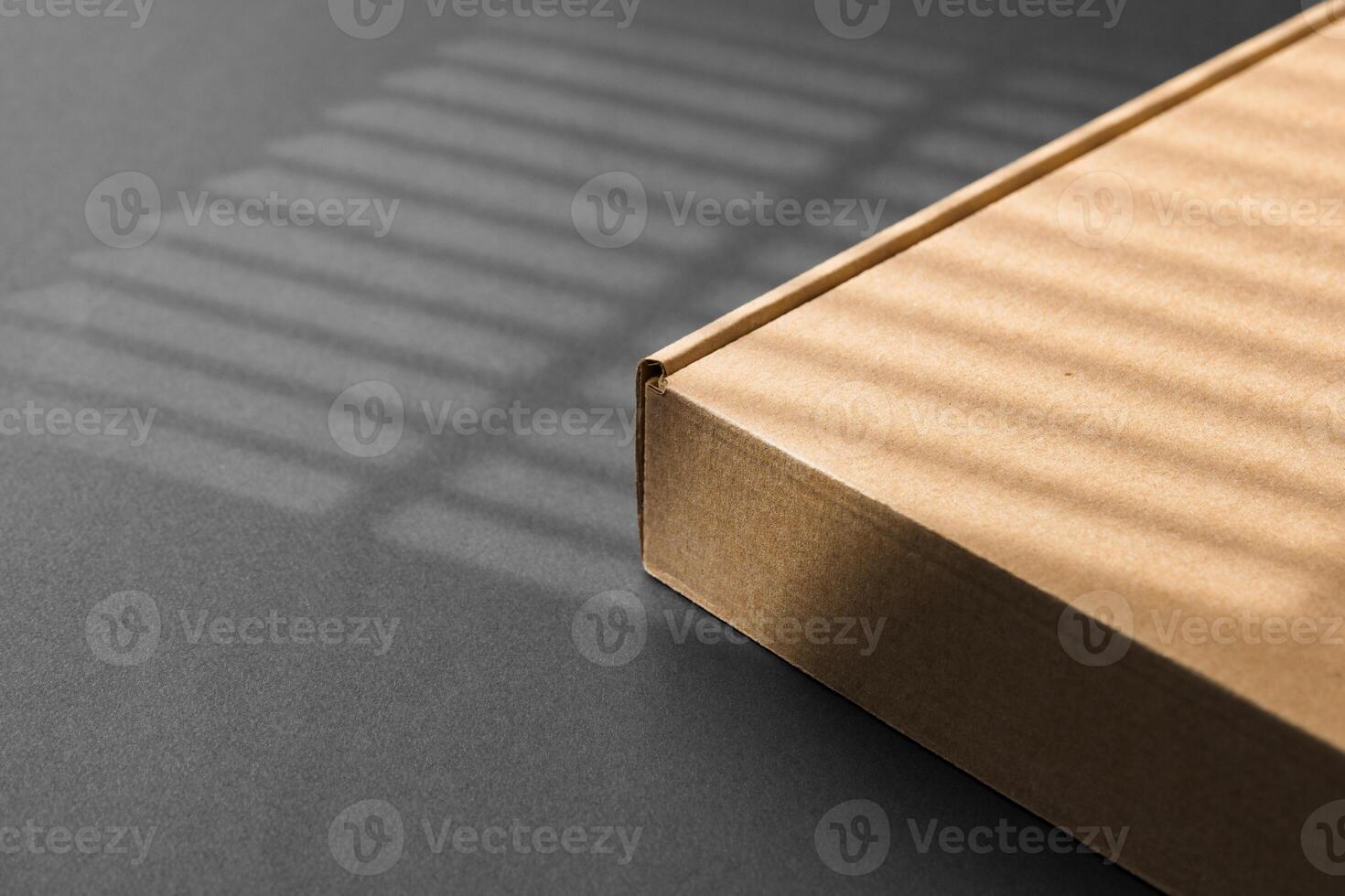 A cardboard box casting shadows on a dark surface in a striped light pattern photo
