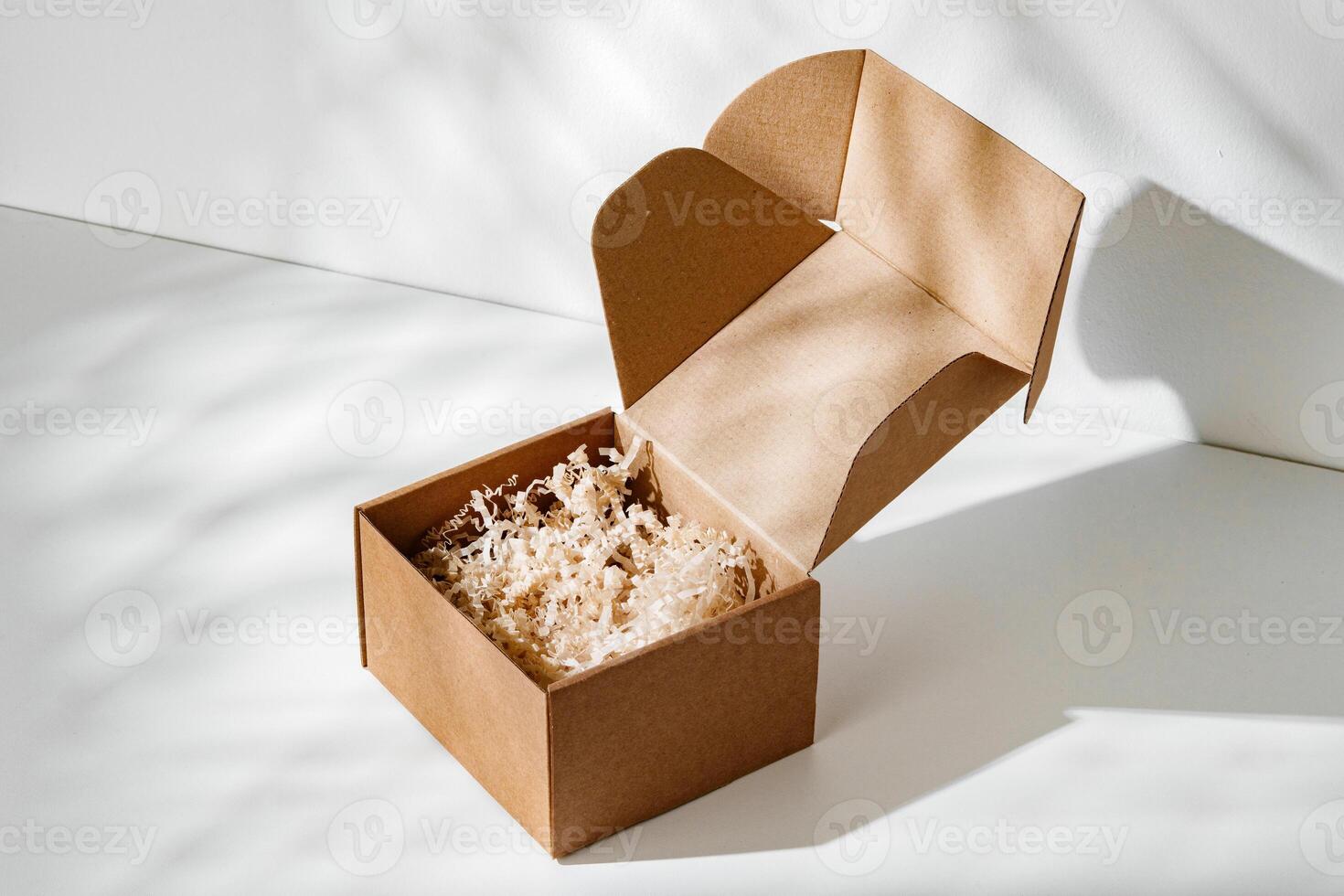 A simple brown gift box with natural filling sits elegantly on a light surface, capturing soft shadows photo