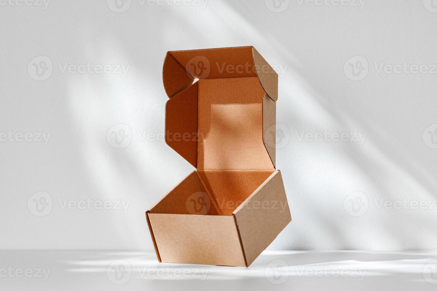 An open cardboard box rests on a bright white surface with soft shadows highlighting its edges and structure in natural light photo