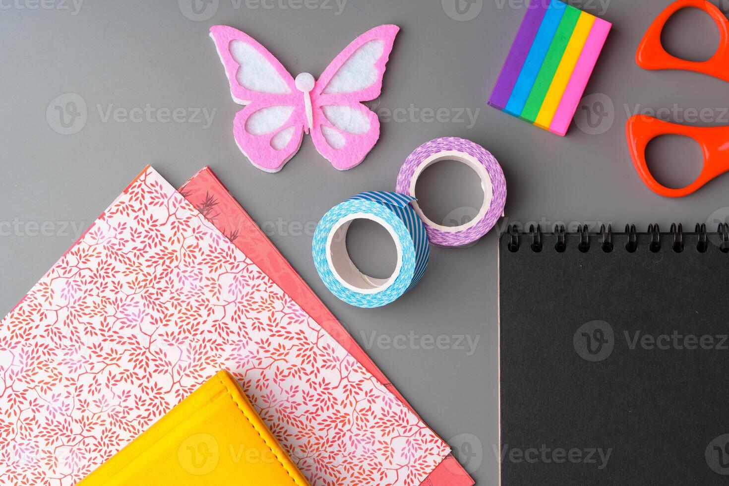 Crafting supplies arranged on a gray surface with a blank notebook, scissors, washi tape, and colorful embellishments photo
