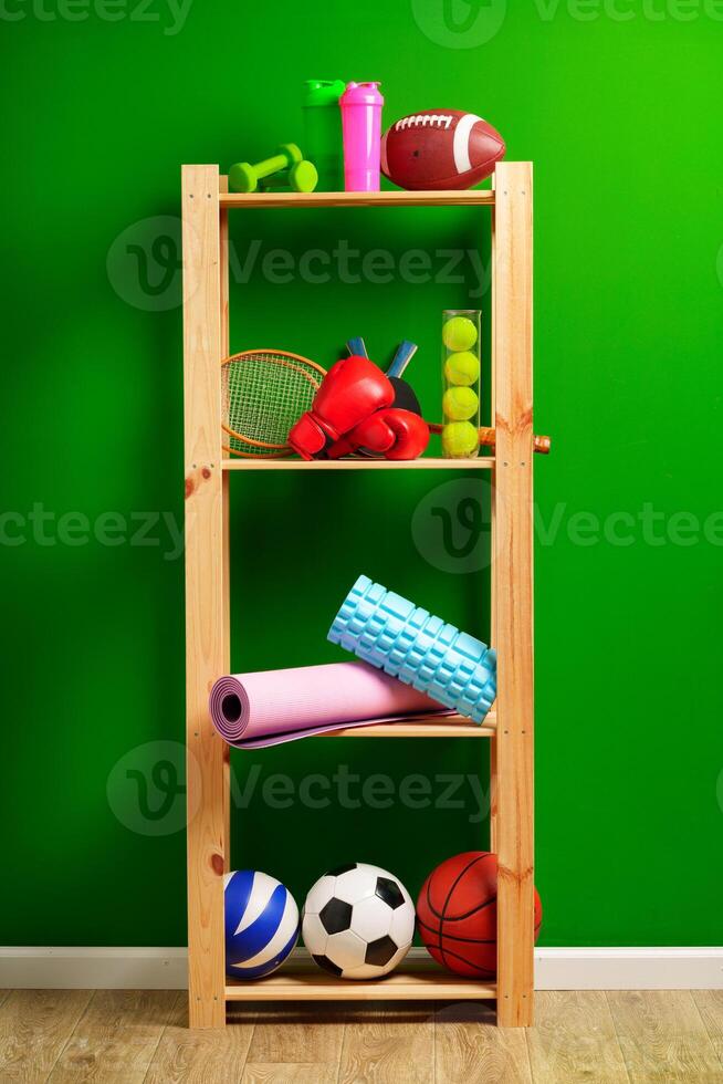 Shelves with different sports equipment against green wall photo