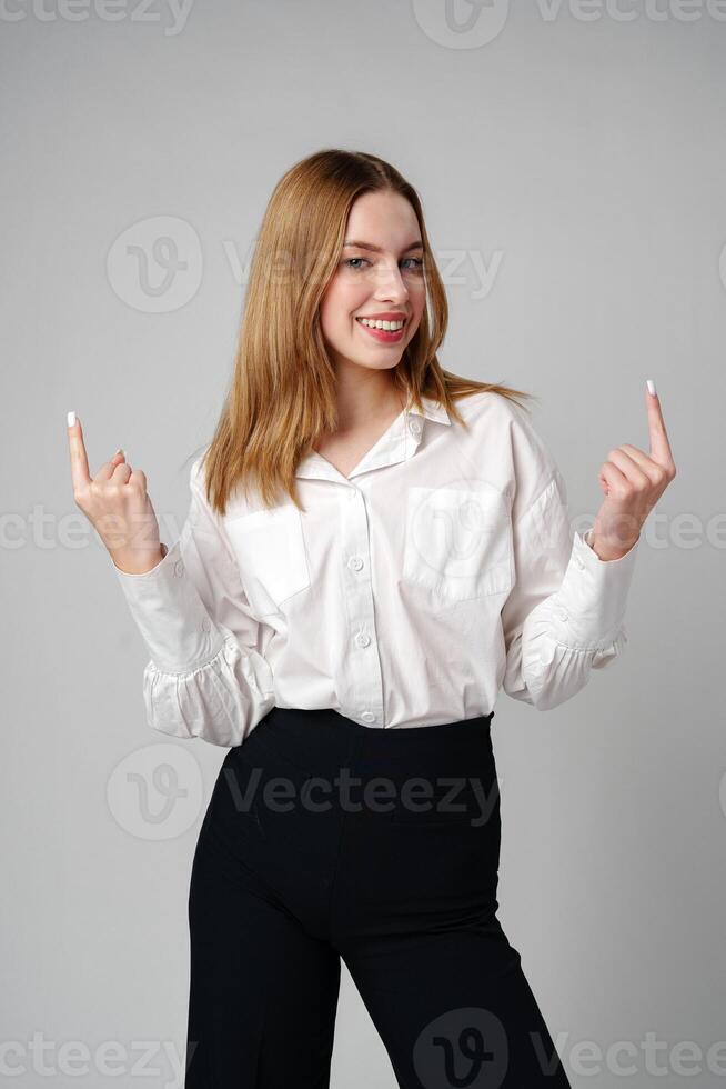 Young businesswoman standing against gray background and pointing her finger to copy space photo