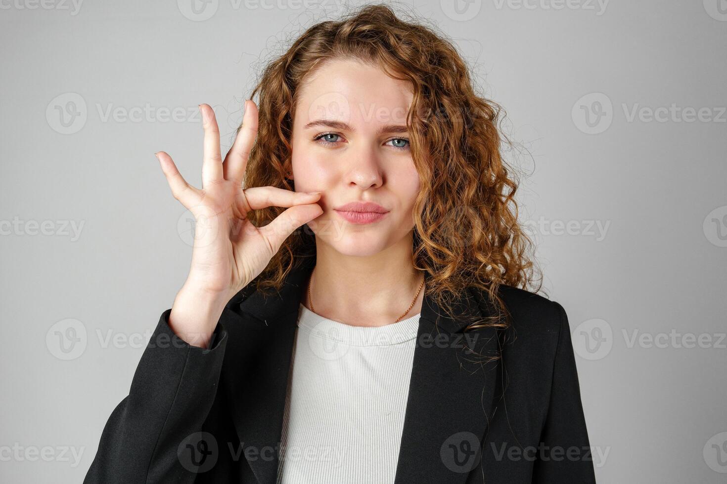 Young Woman Gesturing Silence With Finger on Lips Against a Grey Background photo