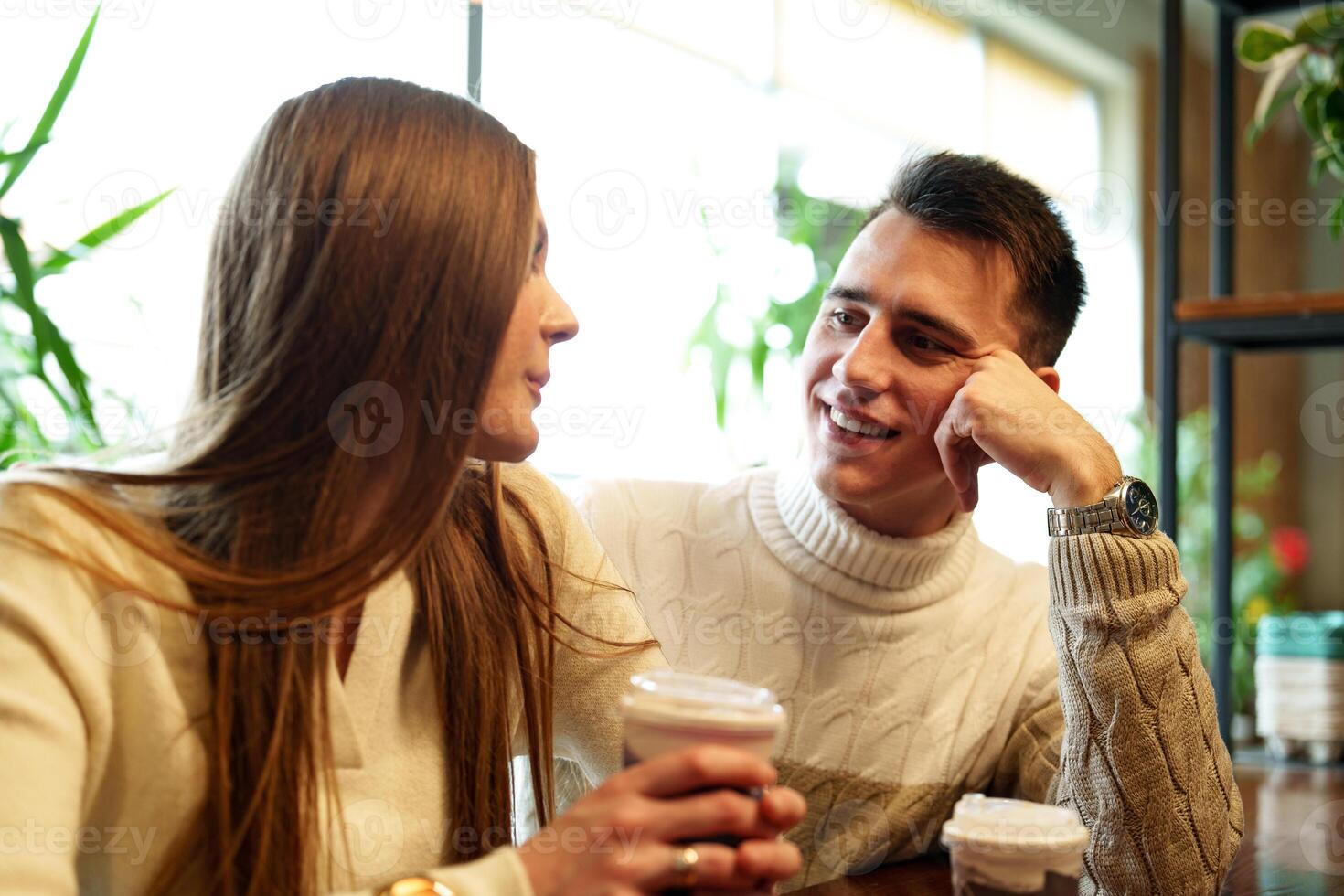 Smiling Couple Enjoying Warm Beverages at a Cozy Cafe on a Sunny Afternoon photo