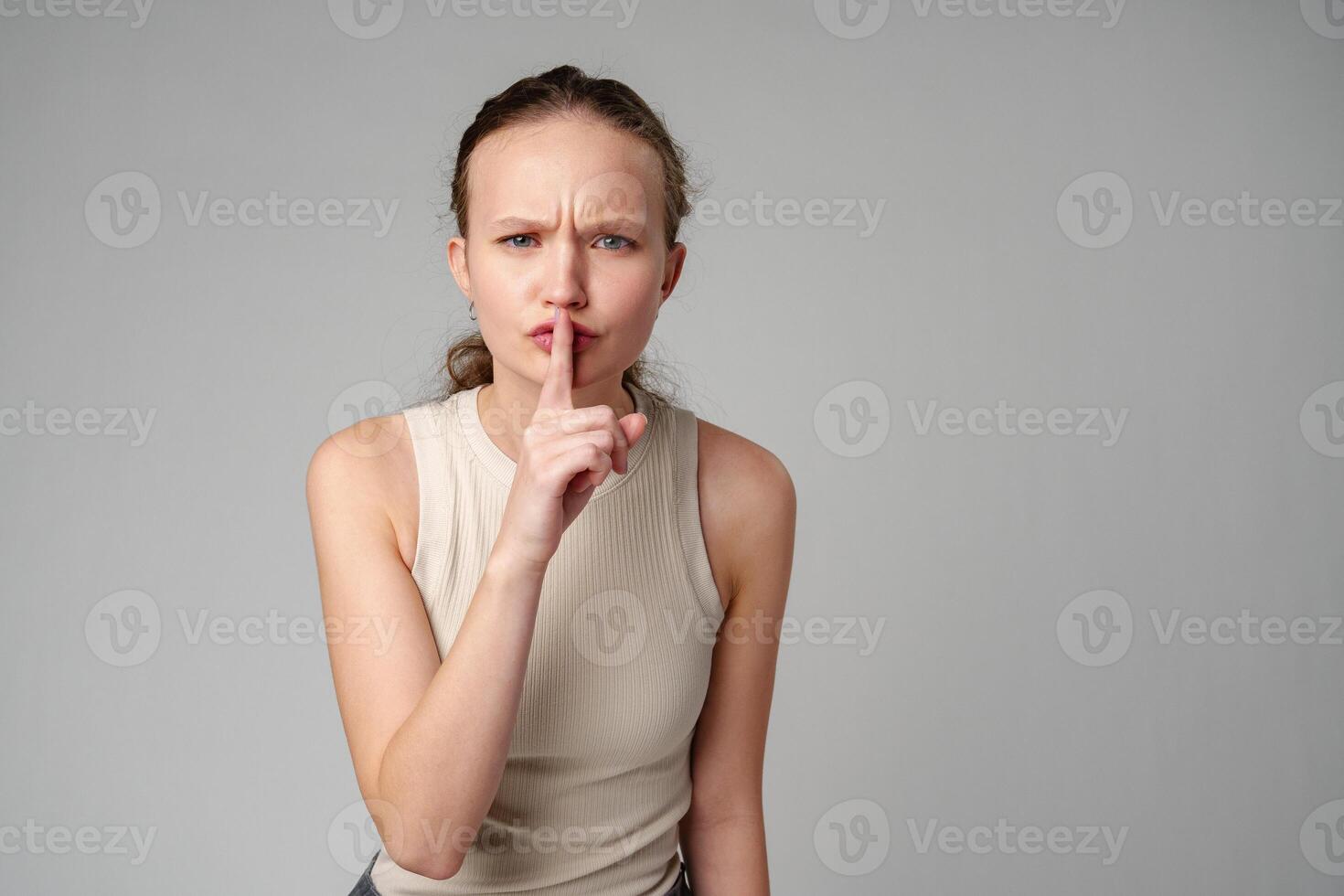Young Woman Making a Hush Gesture on gray background in studio photo