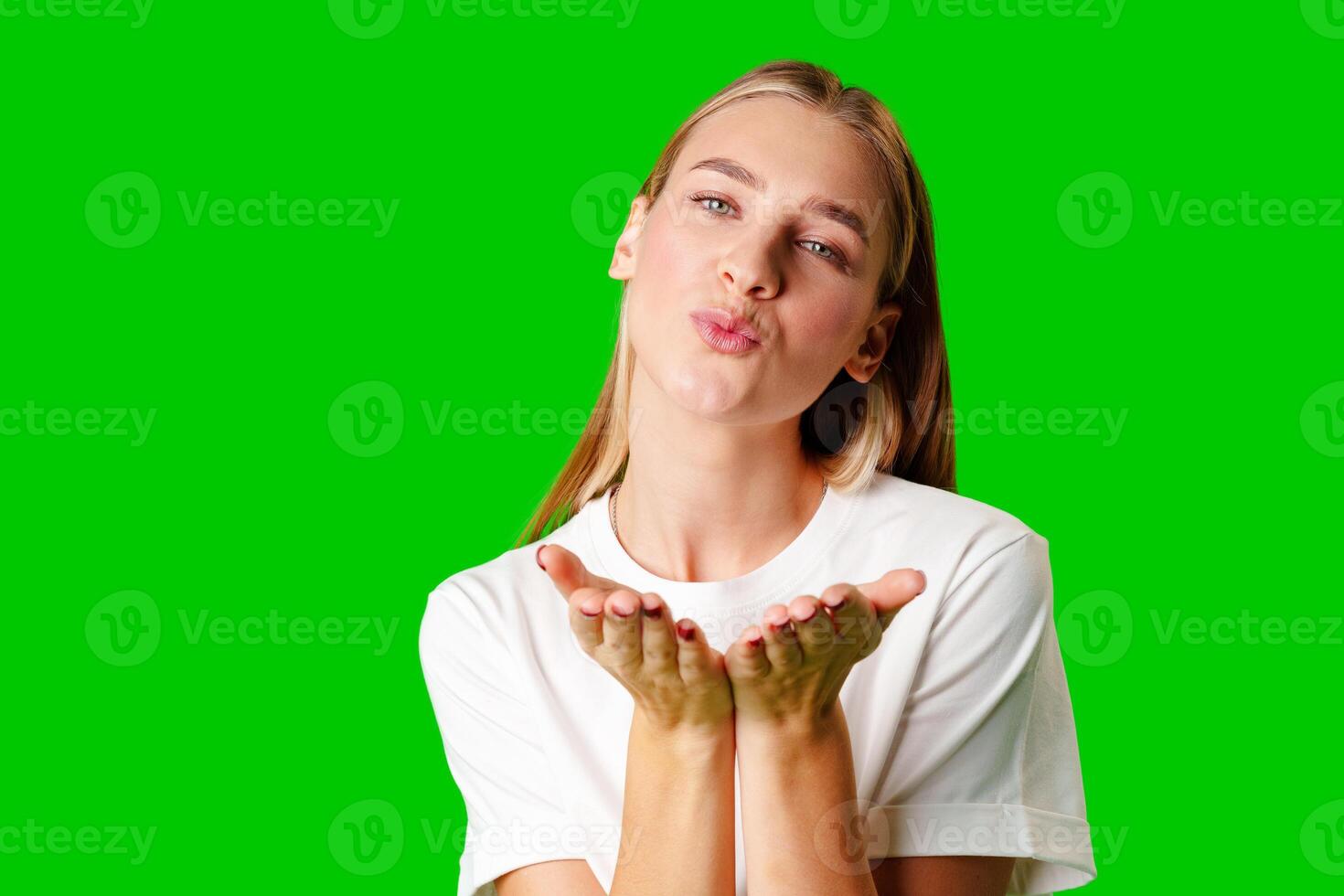 Young Woman Blowing a Kiss With a Playful Expression Against a Bright Green Background photo