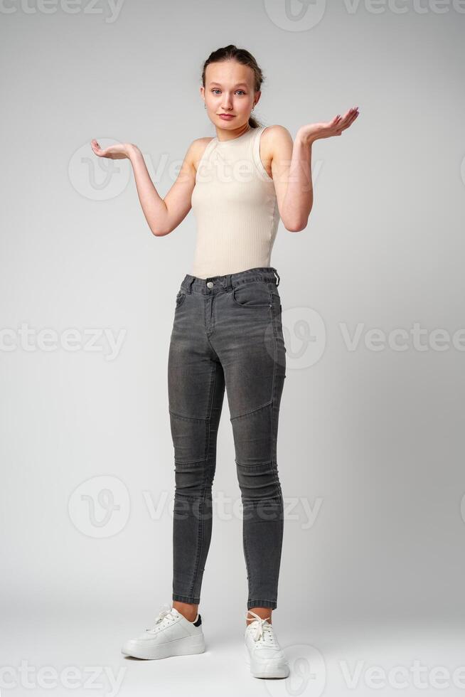 Young Clueless Woman Standing With Outstretched Arms on gray background photo