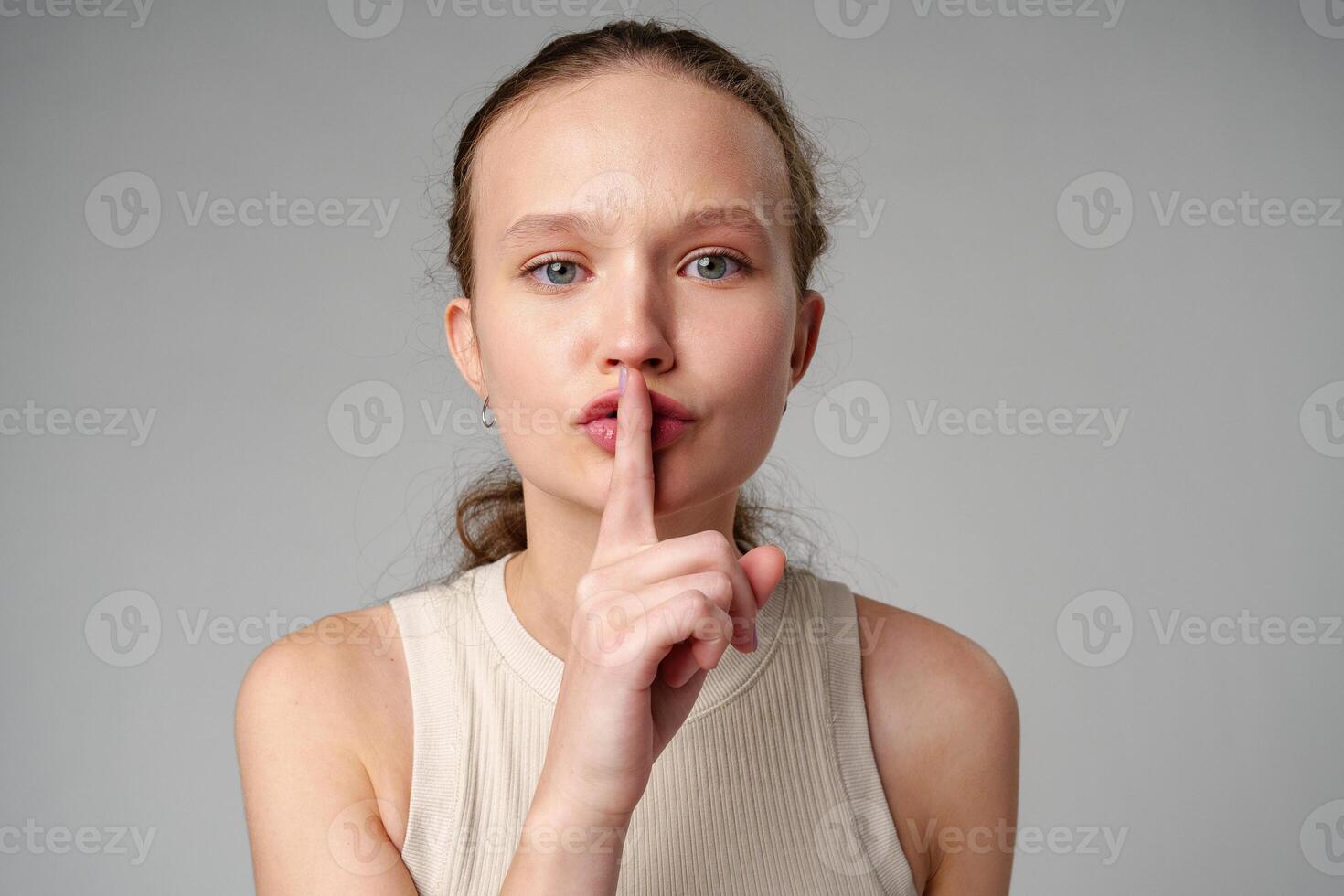 Young Woman Making a Hush Gesture on gray background in studio photo
