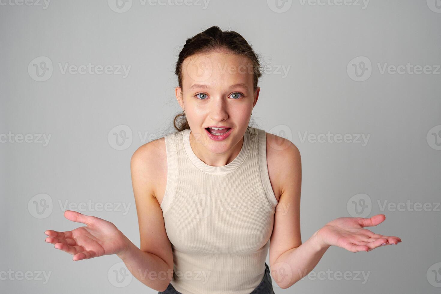 Young Clueless Woman Standing With Outstretched Arms on gray background photo