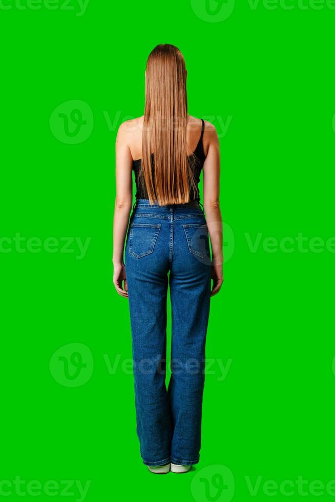 Woman in blue jeans with long hair on green background back view photo