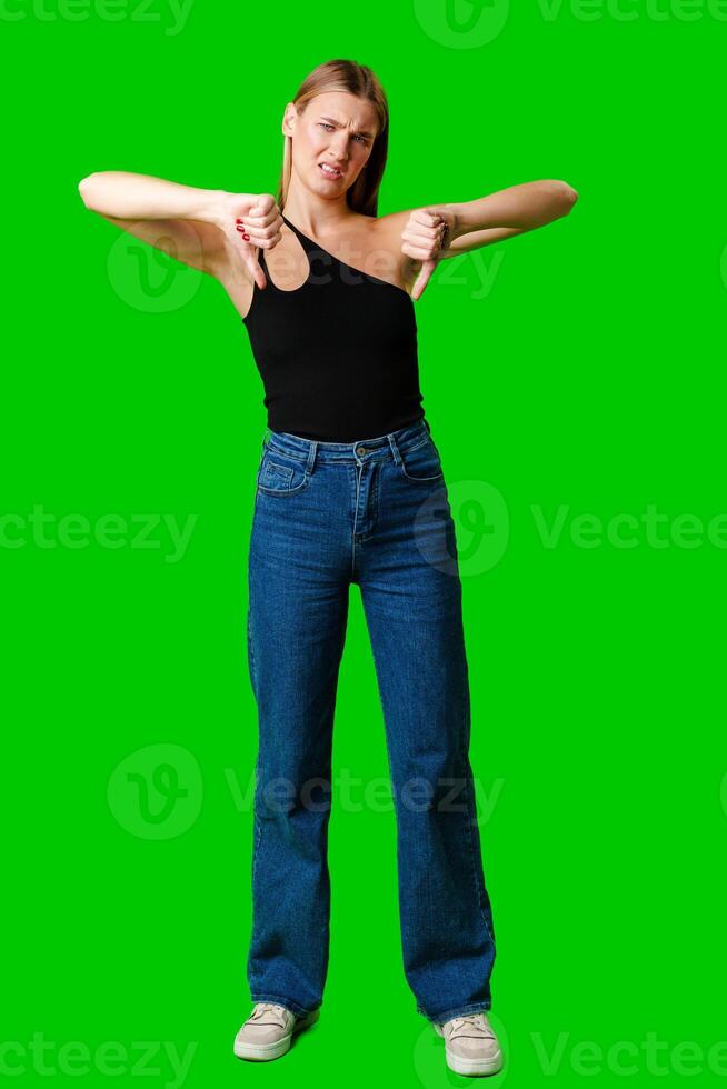 Young Woman Expressing Disapproval With a Thumbs Down Gesture Against a Green Background photo