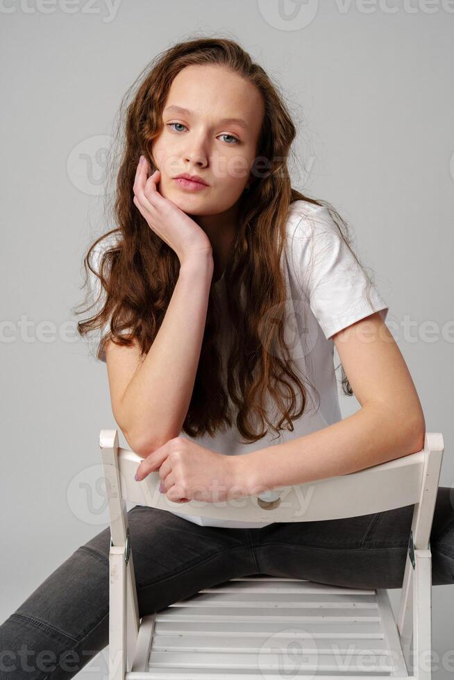 Curly girl model posing on a chair against gray background photo