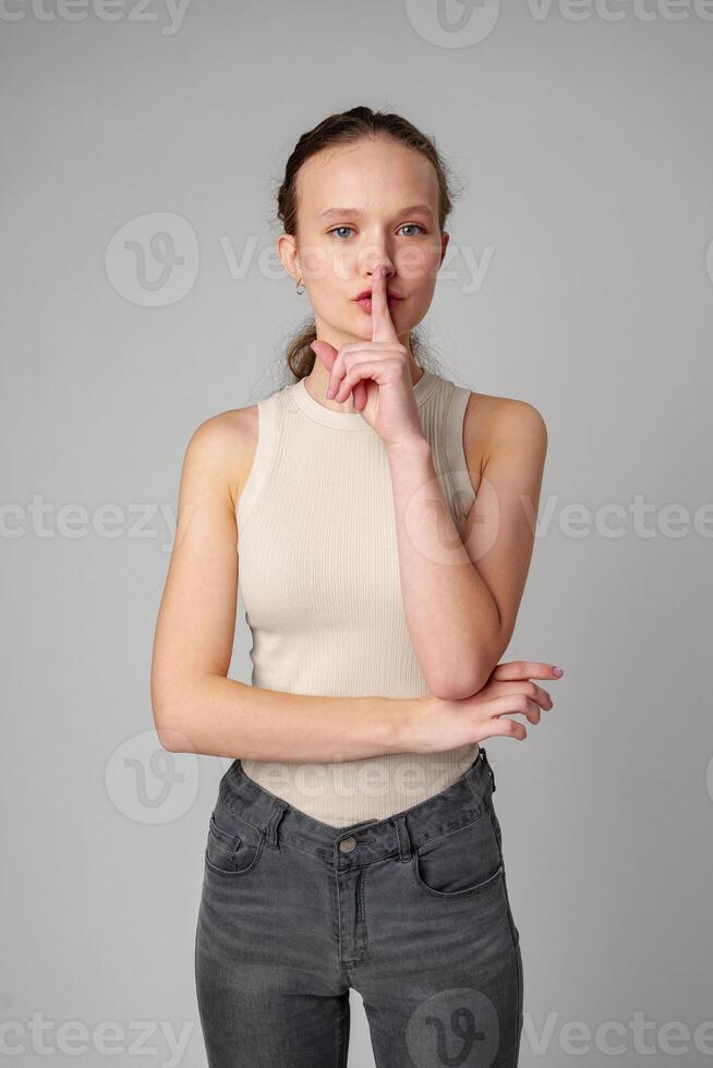 Young Woman Making a Hush Gesture on gray background in studio photo